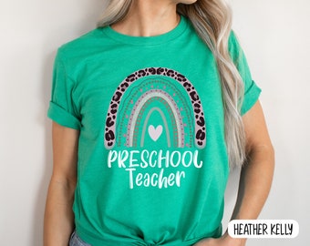 May include: A green t-shirt with a rainbow design and the text "PRESCHOOL Teacher" in white. The rainbow has a pink heart in the center and is decorated with brown leopard print and pink and white dots.