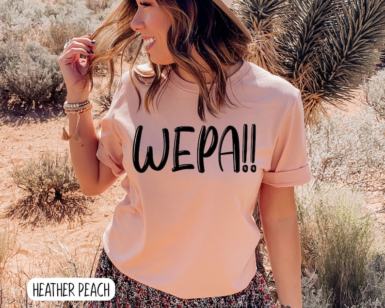 May include: A pink t-shirt with the text "WEPA!" printed in black on the front. The shirt is made of a soft, comfortable material and has a relaxed fit.