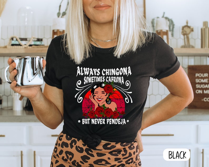 May include: Black t-shirt with a graphic of a woman with red flowers and the text "Always Chingona Sometimes Carrrona - But Never Pendeja -"