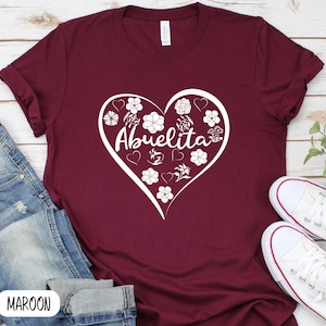 May include: A maroon t-shirt with a white heart design featuring the word "Abuelita" surrounded by flowers and hearts.