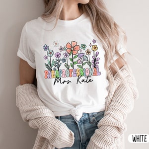 May include: White t-shirt with a colourful floral design and the text "Paraprofessional Mrs. Kate"