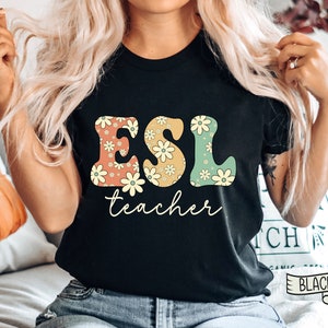 May include: Black t-shirt with the text "ESL teacher" in large, colorful letters with a floral pattern. The letters are in a retro style.