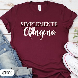 May include: A maroon t-shirt with the text "SIMPLEMENTE Chingona" in white lettering. The text is in a cursive font and includes a small rose graphic.