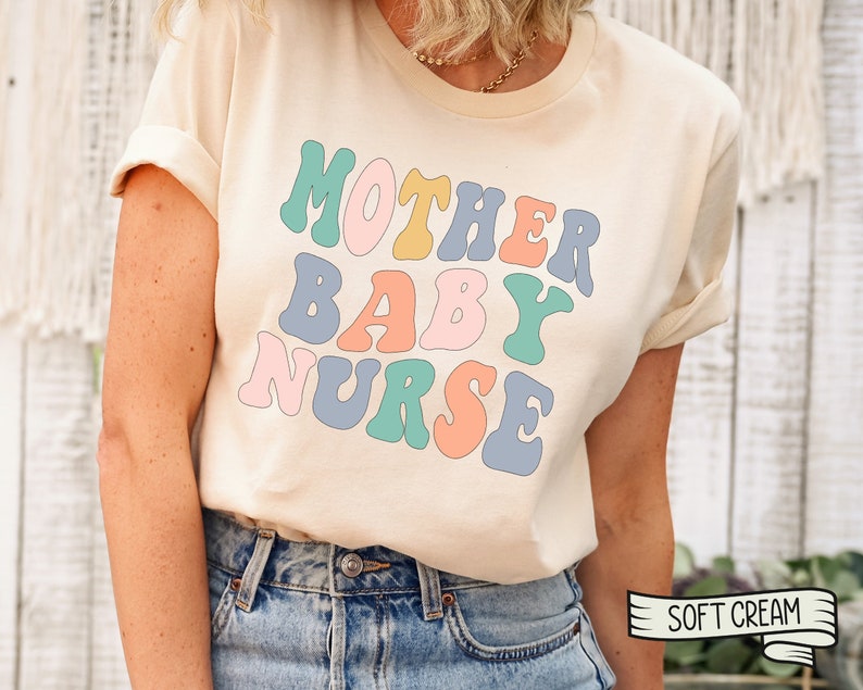 Może przedstawiać: Kremowa koszulka z napisem "MOTHER BABY NURSE" w kolorowym, retro stylu.