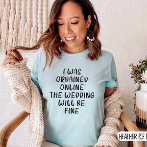 May include: A light blue t-shirt with the text "I was ordained online the wedding will be fine" printed in black.