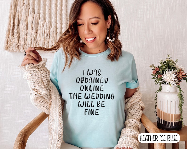 May include: A light blue t-shirt with the text "I was ordained online the wedding will be fine" printed in black.