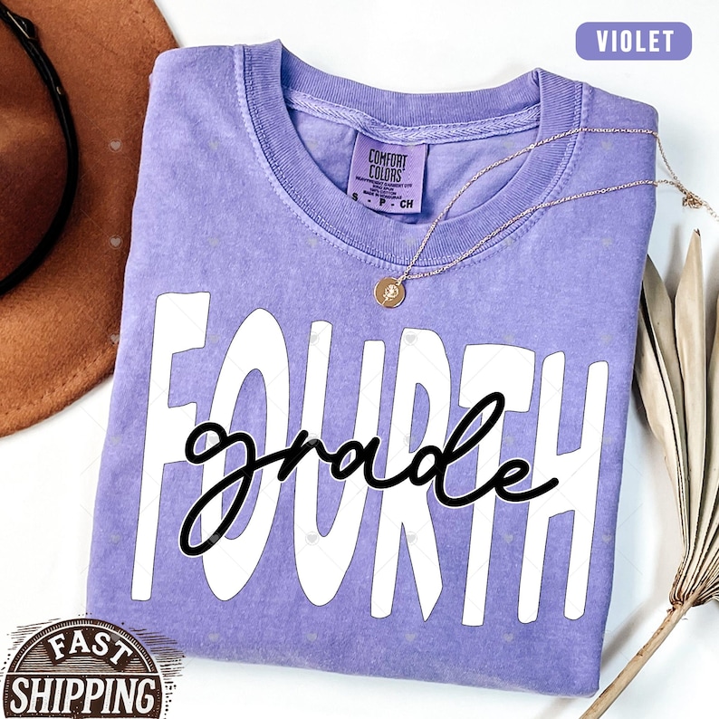 Op de afbeelding: Een paars T-shirt met de tekst "FOURTH grade" in witte letters met een zwarte omtrek. Het shirt is gemaakt van een zacht, comfortabel materiaal.