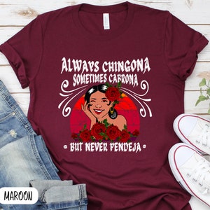 May include: A maroon t-shirt with a graphic of a woman with red roses and the text "Always Chingona Sometimes Carrrona - But Never Pendeja - "