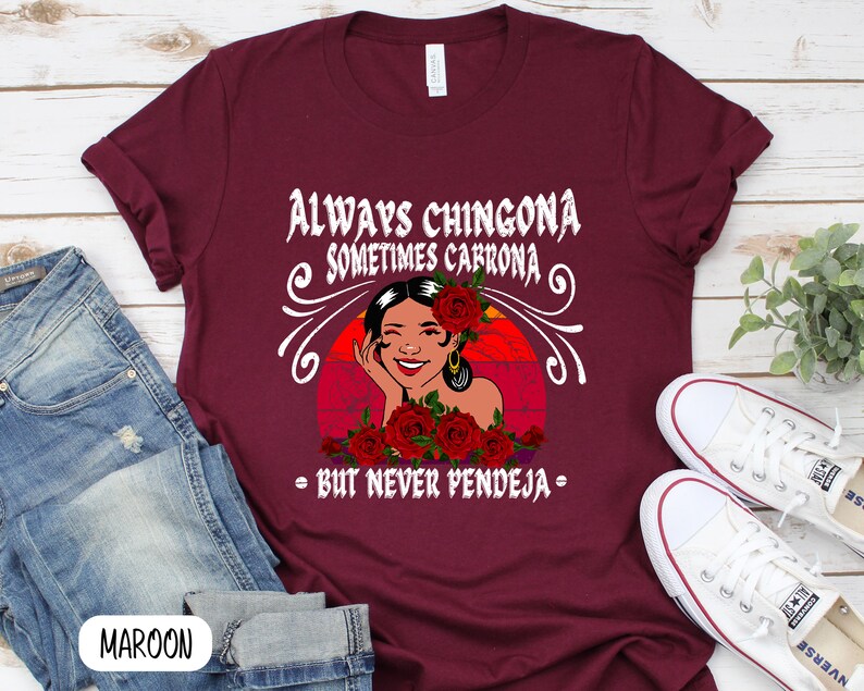 May include: A maroon t-shirt with a graphic of a woman with red roses and the text "Always Chingona Sometimes Carrrona - But Never Pendeja - "