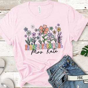 May include: Pink t-shirt with a floral design and the text "Paraprofessional Mrs. Kate" in rainbow letters.