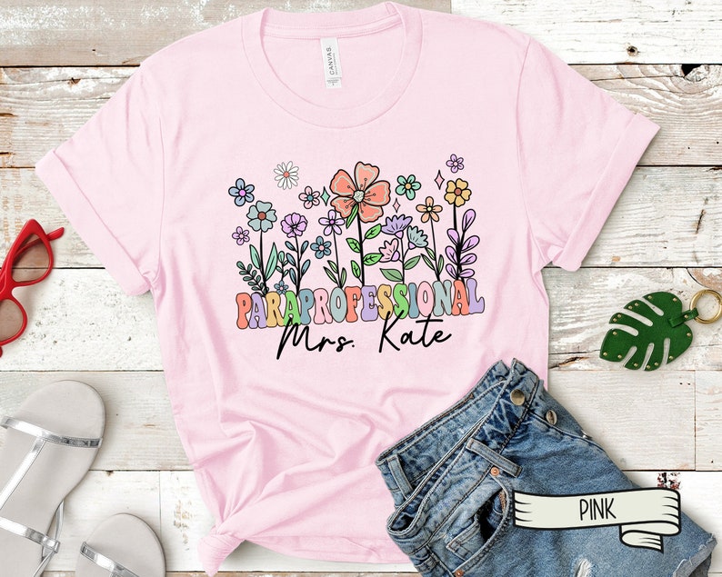 May include: Pink t-shirt with a floral design and the text "Paraprofessional Mrs. Kate" in rainbow letters.