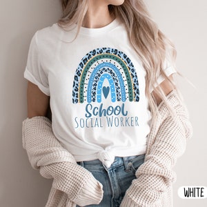 Puede incluir: Camiseta blanca con un dise&ntilde;o de arco&iacute;ris azul y verde y el texto "School Social Worker".