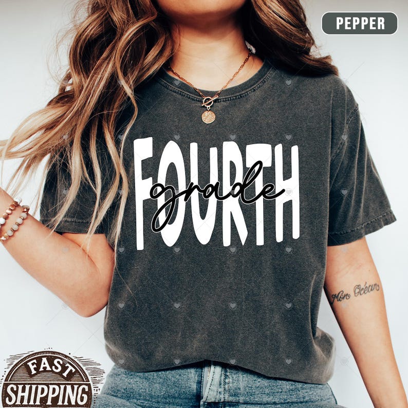 Op de afbeelding: Een grijs T-shirt met de tekst "FOURTH grade" in witte letters. Het shirt wordt gedragen door een persoon met lang bruin haar.
