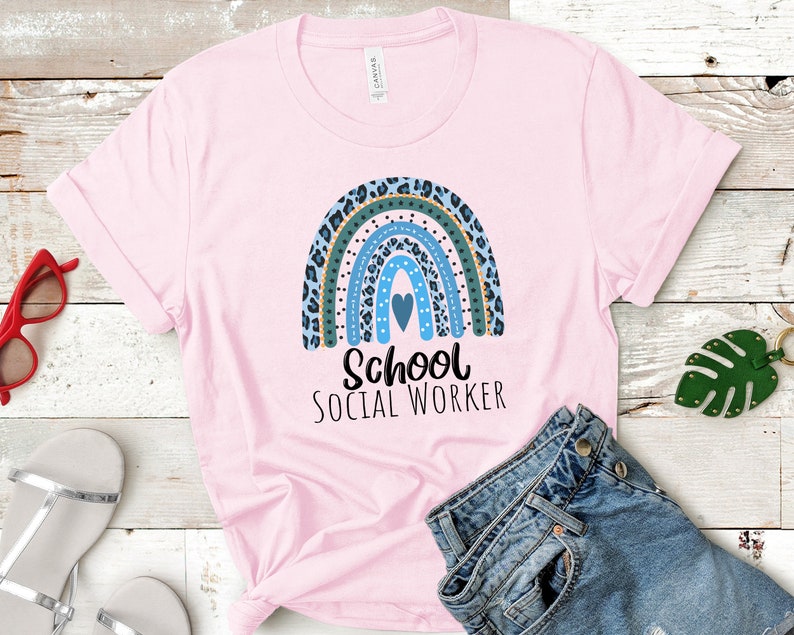 Puede incluir: Camiseta rosa con un dise&ntilde;o de arco&iacute;ris azul, verde y dorado y el texto "School Social Worker".