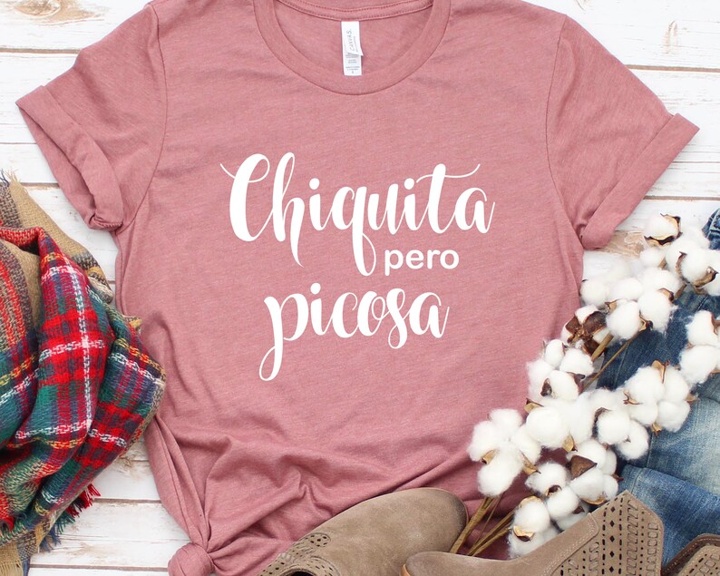 May include: A dusty rose colored t-shirt with the text "Chiquita pero picosa" in white cursive lettering.