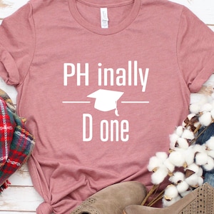 May include: A pink t-shirt with the text "PH inally D one" in white. A graduation cap graphic is above the word "D".