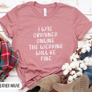 May include: Heather mauve t-shirt with the text "I was ordained online the wedding will be fine" printed in white.