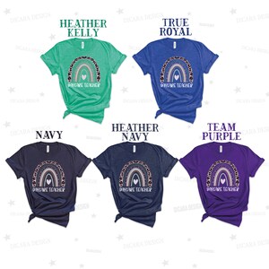 May include: Five t-shirts in different colours, each featuring a rainbow with the text 'Daycare Teacher' printed on the front. The rainbow is decorated with leopard print and a pink heart.