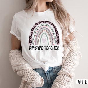 May include: White t-shirt featuring a rainbow design and the text "Daycare Teacher".
