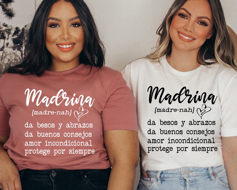 May include: Two women wearing white and pink t-shirts with the word "Madrina" and the definition "[madre-nah] da besos y abrazos da buenos consejos amor incondicional protege por siempre" printed on them.