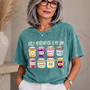 May include: Teal-colored t-shirt with the phrase "EARLY INTERVENTION IS MY JAM" in white. Below the text are illustrations of jam jars, each labeled with a different concept like "Social" and "Cognitive".