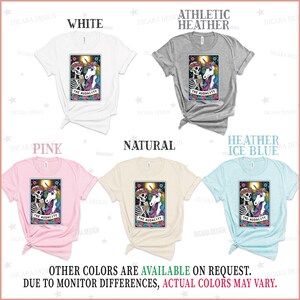 May include: Five t-shirts in different colors with a graphic of a skeleton and a unicorn holding a drink with the text "The Audacity" on a card. The colors are white, athletic heather, pink, natural, and heather ice blue.