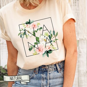 May include: A cream coloured t-shirt with a floral design and the word "NANA" in a black square.