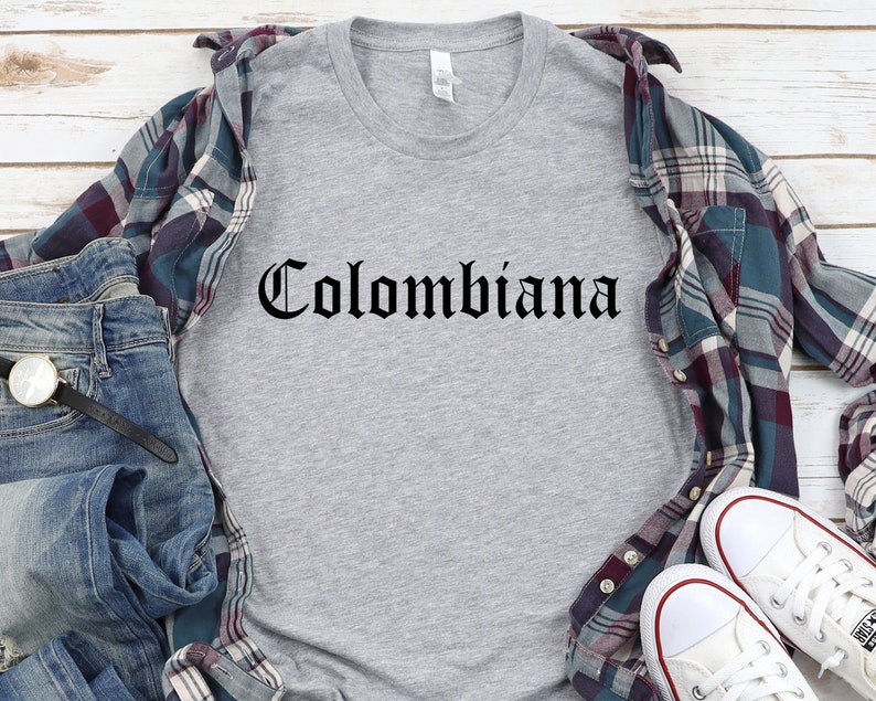 Op de afbeelding: Een grijs T-shirt met het woord "Colombiana" gedrukt in zwarte gotische letters.