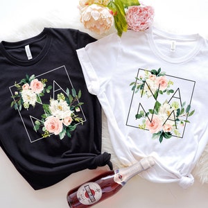 May include: Two t-shirts featuring a floral design and the word "NANA" within a geometric frame. The shirts are black and white.