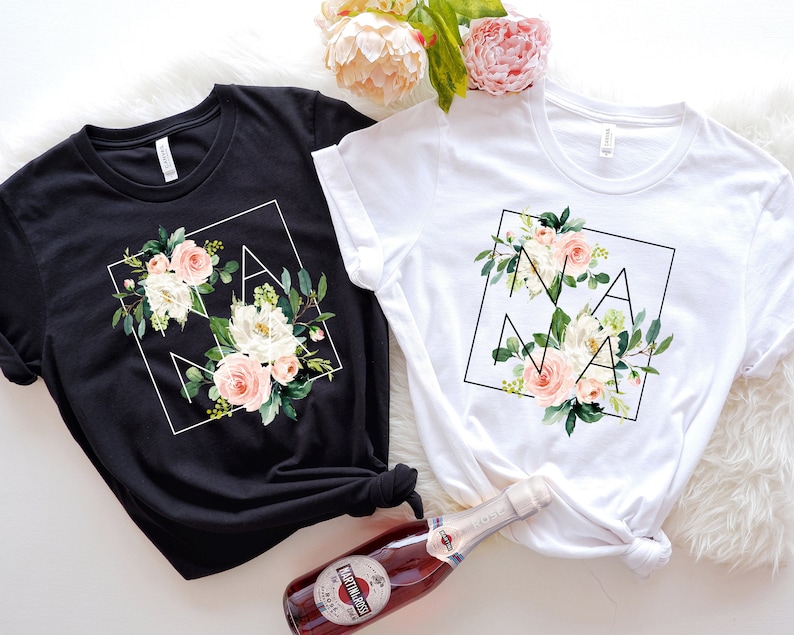 May include: Two t-shirts featuring a floral design and the word "NANA" within a geometric frame. The shirts are black and white.