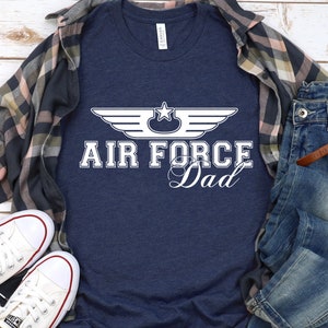 May include: A navy blue t-shirt with a white graphic of an Air Force wing with a star and the text "Air Force Dad".