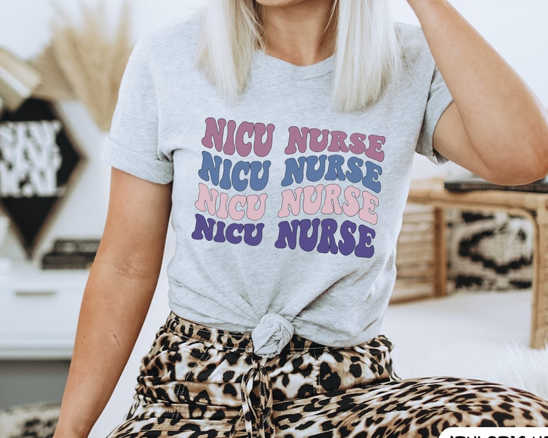 May include: A grey t-shirt with the text "NICU NURSE" repeated four times in a retro font. The text is in shades of pink, blue, and purple.