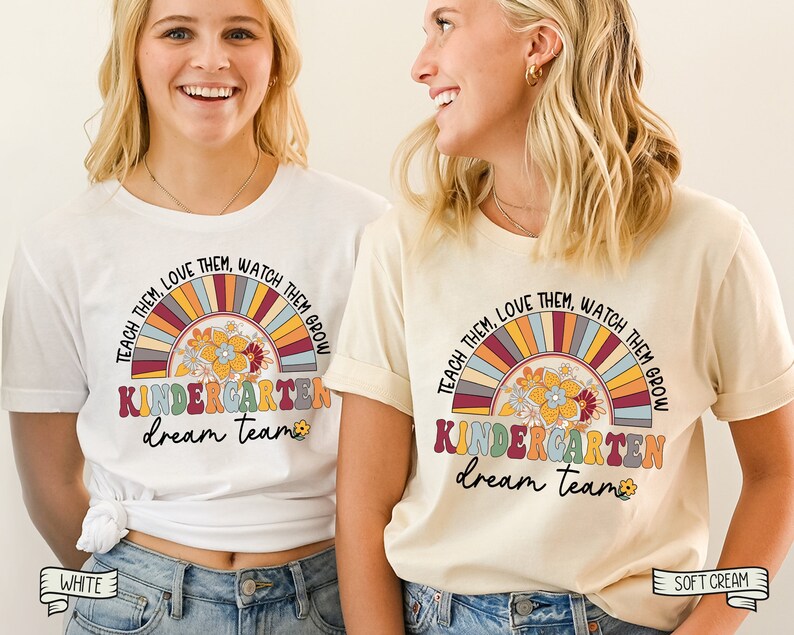 May include: Two white t-shirts with a rainbow design and the text "Teach them, love them, watch them grow. Kindergarten dream team." The t-shirts are on models wearing blue jeans. One t-shirt is white and the other is cream.