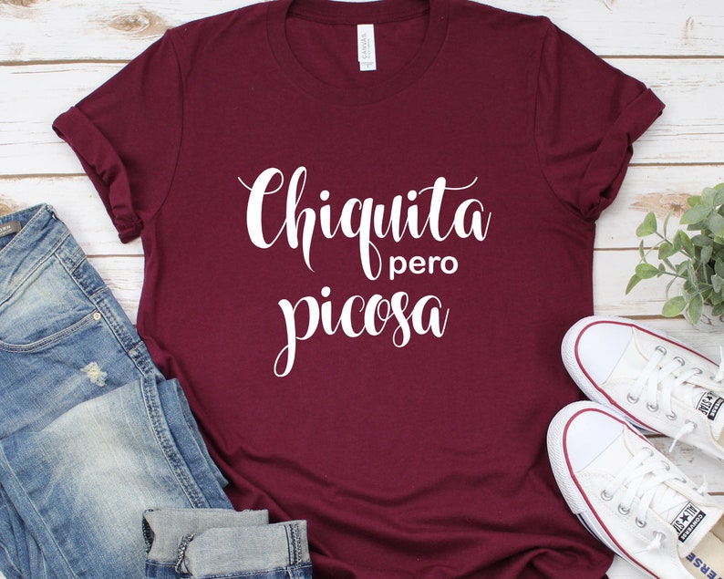 May include: A maroon t-shirt with the text "Chiquita pero picosa" in white cursive lettering.