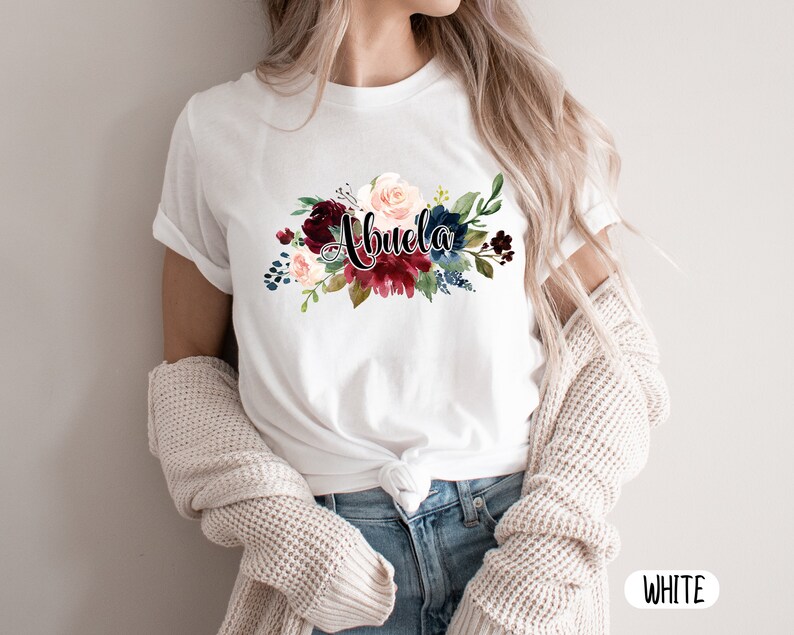 Pu&ograve; includere: Maglietta bianca con un design floreale e la parola "Abuela" in lettere nere.