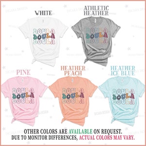 May include: Five t-shirts in different colors with the word "DOULA" printed in a retro style. The colors are white, athletic heather, pink, heather peach, and heather ice blue.