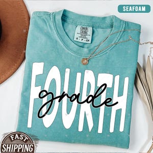 Op de afbeelding: Een turquoise t-shirt met de woorden "FOURTH grade" in witte letters. Het shirt heeft een verweerde look en is gemaakt van een zachte, comfortabele stof.
