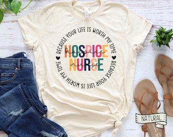 May include: A beige t-shirt with a circle design that says "Because your life is worth my time Hospice Nurse Because your life is worth my time". The text is in black and the circle is filled with colorful stripes.