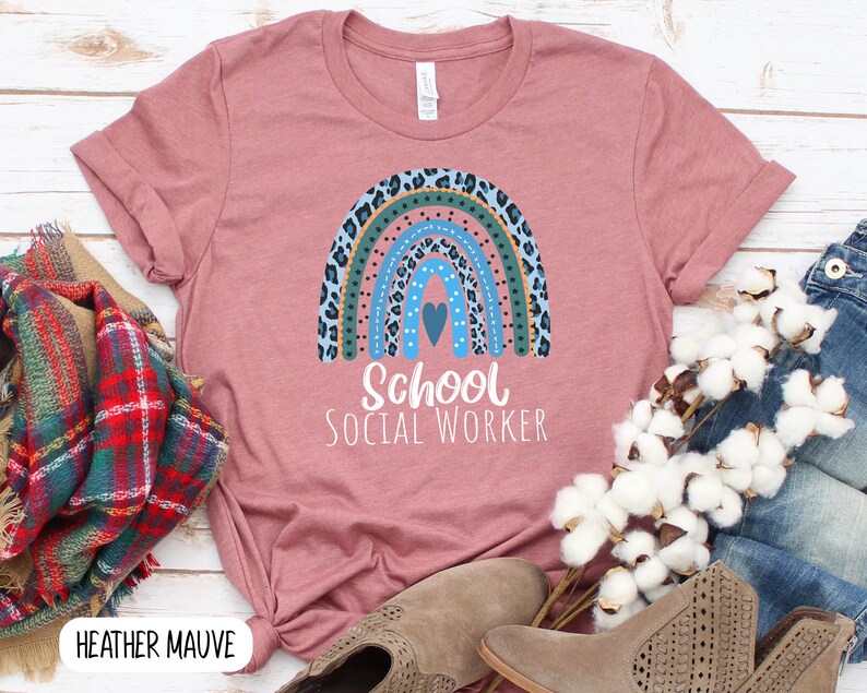 Puede incluir: Una camiseta de color malva claro con un dise&ntilde;o de arco&iacute;ris con estampado de leopardo azul, verde y marr&oacute;n. El arco&iacute;ris tiene un peque&ntilde;o coraz&oacute;n azul en el centro. El texto "School Social Worker" est&aacute; impreso debajo del arco&iacute;ris.
