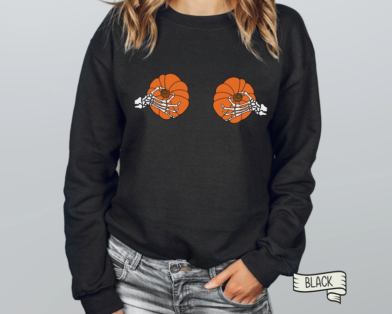 Op de afbeelding: Zwart sweatshirt met een afbeelding van twee skeletten die pompoenen vasthouden. De tekst "BLACK" is gedrukt op een wit lint.