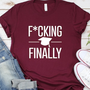 May include: A maroon t-shirt with white text that reads "F*CKING FINALLY" with a graduation cap graphic above the word "FINALLY".