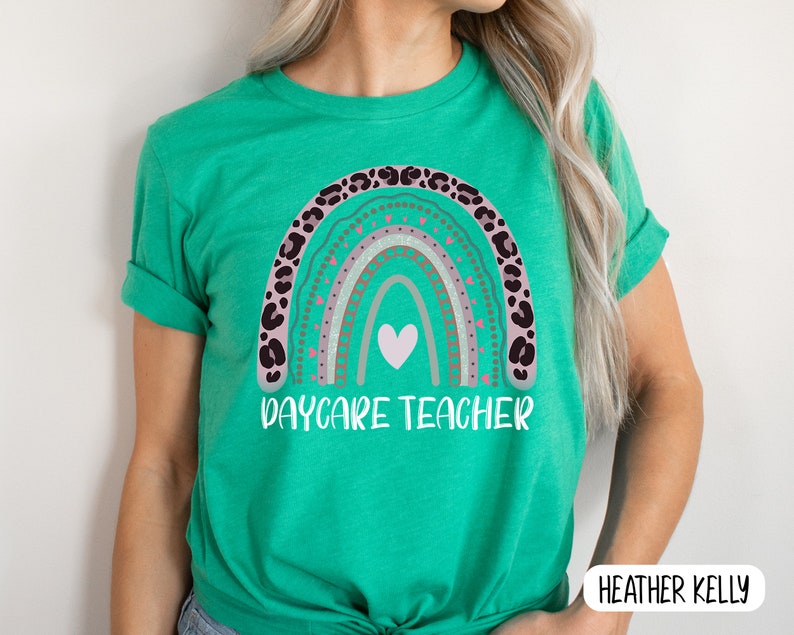 May include: A green t-shirt featuring a rainbow design and the text "Daycare Teacher". The rainbow is decorated with pink, brown, and white accents.