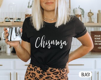 May include: Black t-shirt with the word "Chismosa" written in white cursive lettering.