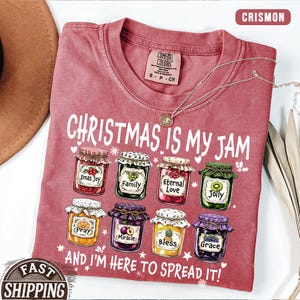 May include: Crimson Comfort Colors t-shirt with the phrase "Christmas is My Jam" and images of jam jars. The jars have labels like "Xmas Joy" and "Grace". The shirt also says "And I'm Here to Spread It!"