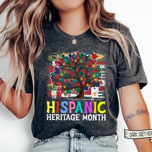 May include: A dark grey heather t-shirt with a colorful handprint tree design and the text "HISPANIC HERITAGE MONTH".