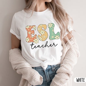 May include: White t-shirt with a floral design that spells out "ESL teacher".