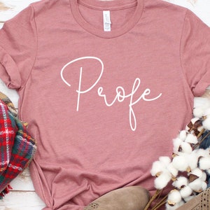 May include: A dusty rose colored t-shirt with the word "Profe" written in white cursive script.