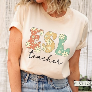May include: A cream colored t-shirt with a floral design that spells out "ESL teacher" in a retro font.