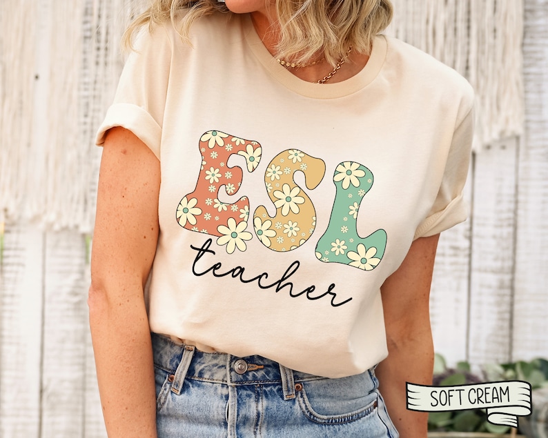 May include: A cream colored t-shirt with a floral design that spells out "ESL teacher" in a retro font.