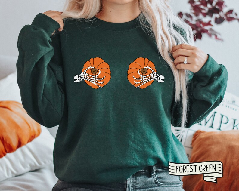 Op de afbeelding: Groen sweatshirt met een afbeelding van twee pompoenen met skeletten die ze vasthouden. De tekst "FOREST GREEN" staat op een wit lint in de rechterbenedenhoek van de afbeelding.